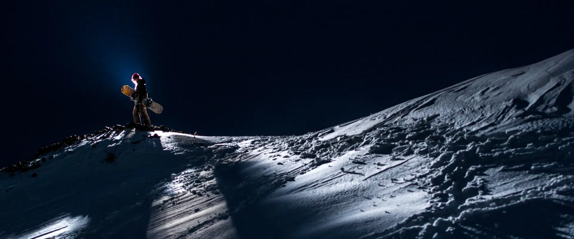 Snowboarder standing at the top of Boreal Mountain at night