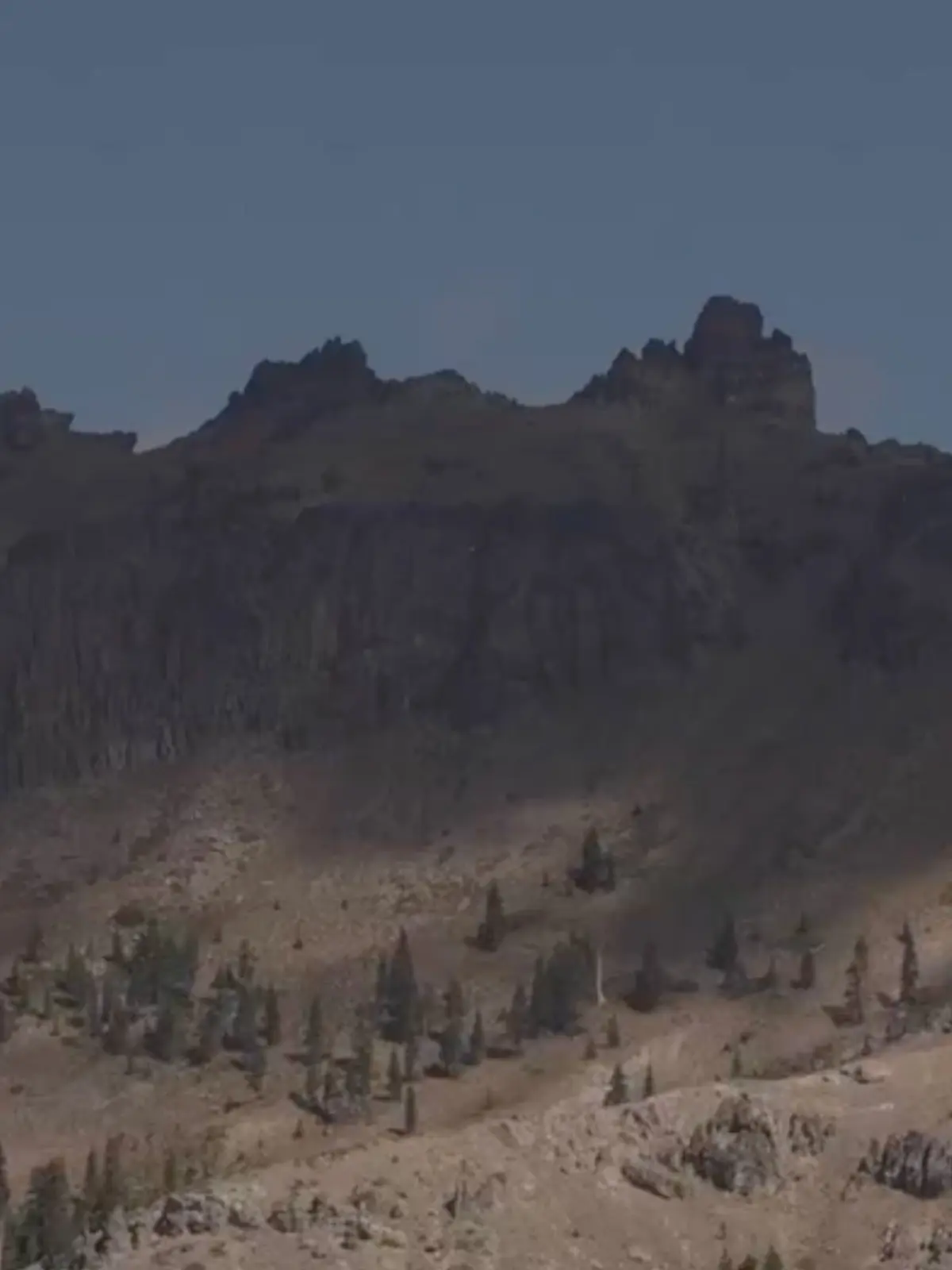 View of the rocky Castle Peak ridgeline with sparse trees beneath a blue sky.